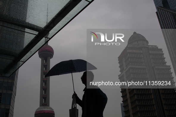 A man is walking with an umbrella as the Oriental Pearl TV Tower is seen in the background in Shanghai, China, on June 25, 2024, as China is...