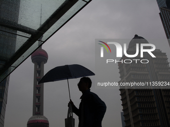 A man is walking with an umbrella as the Oriental Pearl TV Tower is seen in the background in Shanghai, China, on June 25, 2024, as China is...