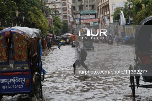 A schoolboy is walking through a waterlogged road during heavy rainfall in Dhaka, Bangladesh, on June 26, 2024. 