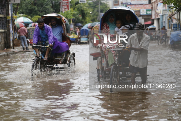 Rickshaw pullers are making their way through a waterlogged road following heavy rainfall in Dhaka, Bangladesh, on June 26, 2024. 