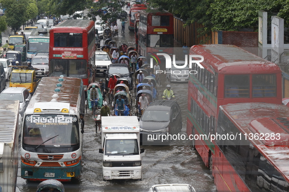 People are making their way through a waterlogged street during heavy rainfall in Dhaka, Bangladesh, on June 26, 2024. 