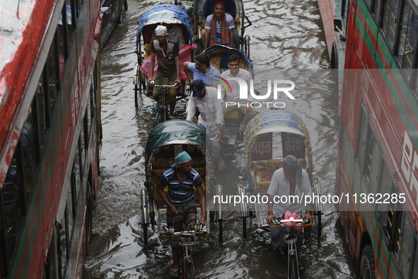 Rickshaw pullers are making their way through a waterlogged street during heavy rainfall in Dhaka, Bangladesh, on June 26, 2024. 