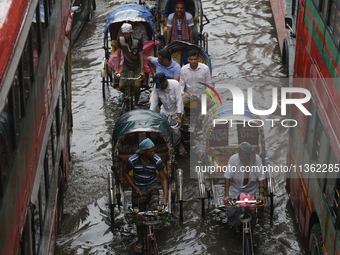 Rickshaw pullers are making their way through a waterlogged street during heavy rainfall in Dhaka, Bangladesh, on June 26, 2024. (