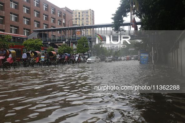 Rickshaw pullers are making their way through a waterlogged street during heavy rainfall in Dhaka, Bangladesh, on June 26, 2024. 