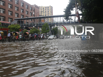 Rickshaw pullers are making their way through a waterlogged street during heavy rainfall in Dhaka, Bangladesh, on June 26, 2024. (