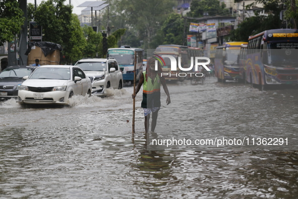 A city corporation cleaner is walking through a waterlogged street during heavy rainfall in Dhaka, Bangladesh, on June 26, 2024. 