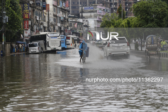 A delivery man is riding a bicycle through a waterlogged street during heavy rainfall in Dhaka, Bangladesh, on June 26, 2024. 