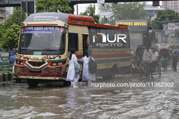 People are making their way through a waterlogged street during heavy rainfall in Dhaka, Bangladesh, on June 26, 2024. 