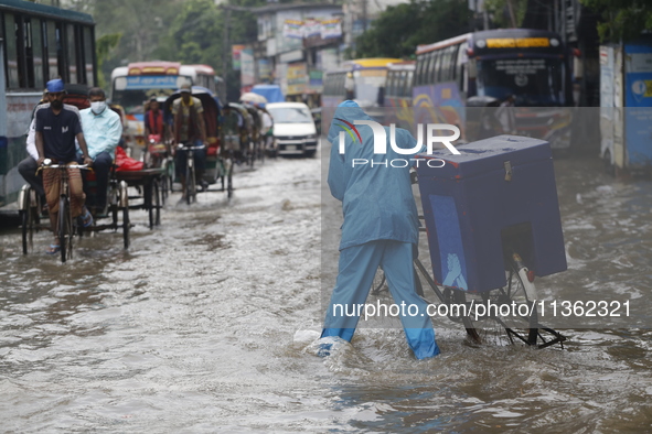 A delivery man is walking through a waterlogged street during heavy rainfall in Dhaka, Bangladesh, on June 26, 2024. 