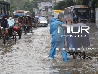 A delivery man is walking through a waterlogged street during heavy rainfall in Dhaka, Bangladesh, on June 26, 2024. (