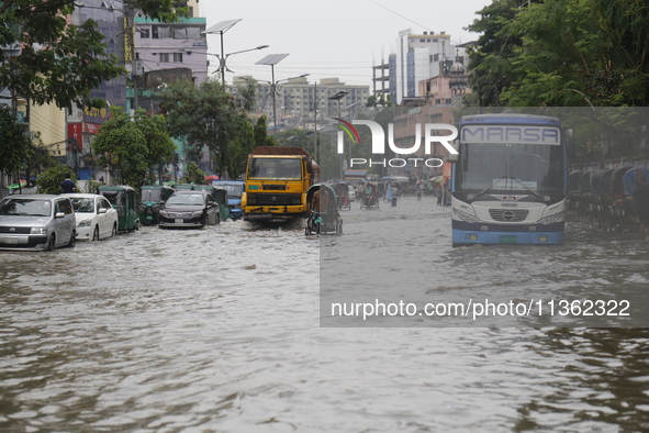 People are making their way through a waterlogged street during heavy rainfall in Dhaka, Bangladesh, on June 26, 2024. 