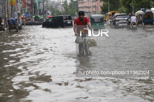 A man is riding a bicycle through a waterlogged street during heavy rainfall in Dhaka, Bangladesh, on June 26, 2024. 