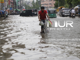 A man is riding a bicycle through a waterlogged street during heavy rainfall in Dhaka, Bangladesh, on June 26, 2024. (