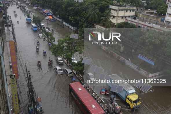 People are making their way through a waterlogged street during heavy rainfall in Dhaka, Bangladesh, on June 26, 2024. 