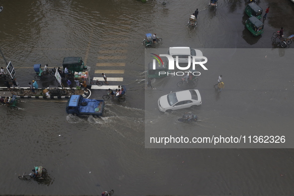 People are making their way through a waterlogged street during heavy rainfall in Dhaka, Bangladesh, on June 26, 2024. 