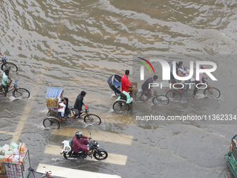 People are making their way through a waterlogged street during heavy rainfall in Dhaka, Bangladesh, on June 26, 2024. (