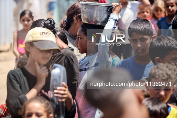 Displaced Palestinian children are waiting for food being distributed at a camp for internally displaced people where they are living due to...