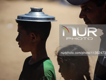 Displaced Palestinian children are waiting for food being distributed at a camp for internally displaced people where they are living due to...