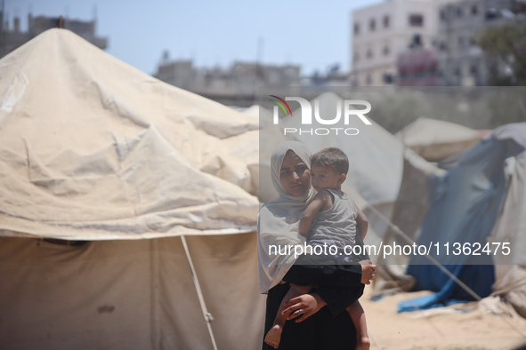 A displaced Palestinian woman is carrying her child outside her tent in Deir el-Balah, on June 26, 2024, amid the ongoing conflict between I...