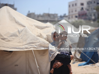 A displaced Palestinian woman is carrying her child outside her tent in Deir el-Balah, on June 26, 2024, amid the ongoing conflict between I...