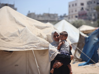 A displaced Palestinian woman is carrying her child outside her tent in Deir el-Balah, on June 26, 2024, amid the ongoing conflict between I...