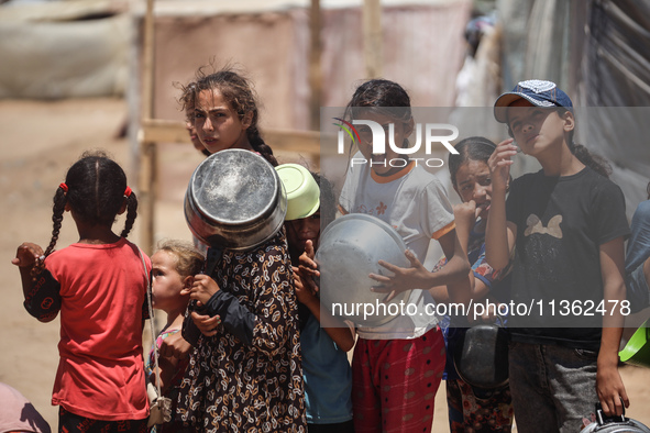 Displaced Palestinian children are waiting for food being distributed at a camp for internally displaced people where they are living due to...