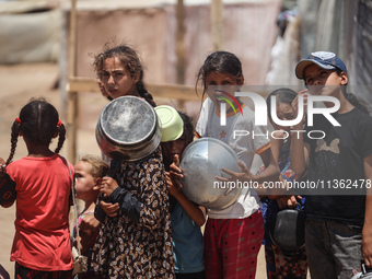 Displaced Palestinian children are waiting for food being distributed at a camp for internally displaced people where they are living due to...