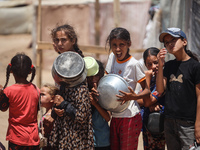 Displaced Palestinian children are waiting for food being distributed at a camp for internally displaced people where they are living due to...