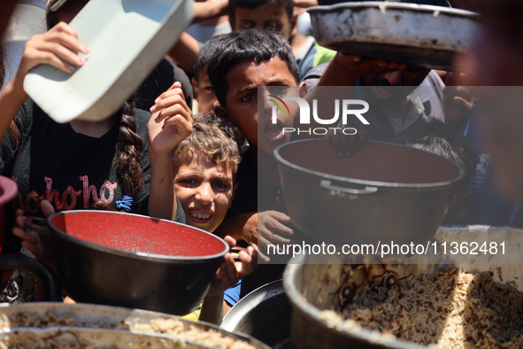 Displaced Palestinian children are waiting for food being distributed at a camp for internally displaced people where they are living due to...