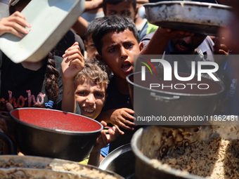 Displaced Palestinian children are waiting for food being distributed at a camp for internally displaced people where they are living due to...