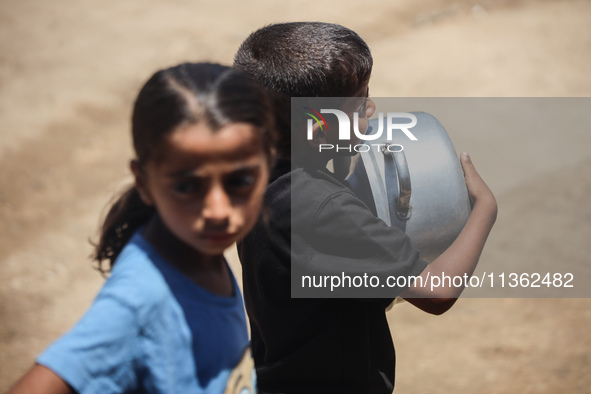 Displaced Palestinian children are waiting for food being distributed at a camp for internally displaced people where they are living due to...