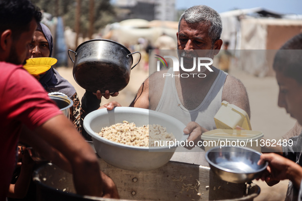 Displaced Palestinian children are waiting for food being distributed at a camp for internally displaced people where they are living due to...