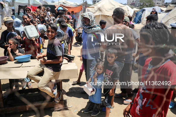 Displaced Palestinian children are waiting for food being distributed at a camp for internally displaced people where they are living due to...