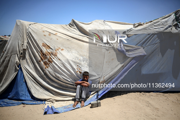 A displaced Palestinian boy is sitting in front of his tent in Deir el-Balah, on June 26, 2024, amid the ongoing conflict between Israel and...