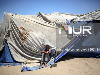 A displaced Palestinian boy is sitting in front of his tent in Deir el-Balah, on June 26, 2024, amid the ongoing conflict between Israel and...