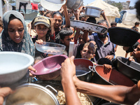 Displaced Palestinian children are waiting for food being distributed at a camp for internally displaced people where they are living due to...