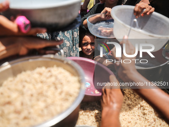 Displaced Palestinian children are waiting for food being distributed at a camp for internally displaced people where they are living due to...