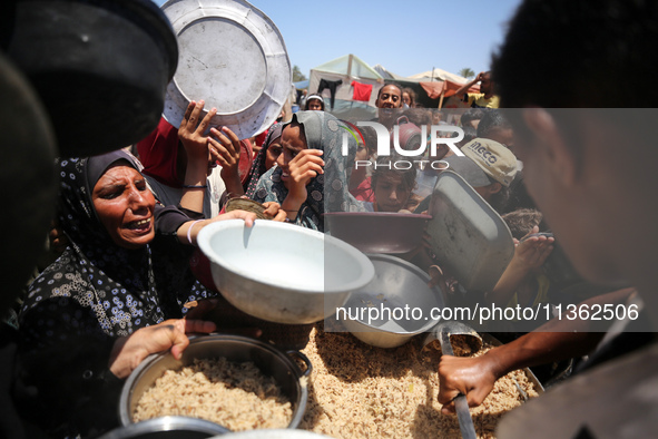 Displaced Palestinian children are waiting for food being distributed at a camp for internally displaced people where they are living due to...