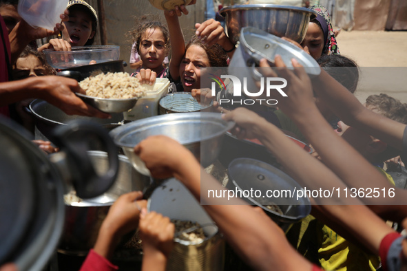 Displaced Palestinian children are waiting for food being distributed at a camp for internally displaced people where they are living due to...