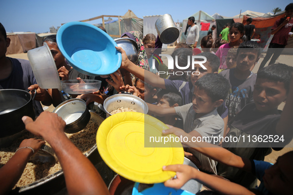 Displaced Palestinian children are waiting for food being distributed at a camp for internally displaced people where they are living due to...