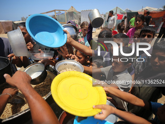 Displaced Palestinian children are waiting for food being distributed at a camp for internally displaced people where they are living due to...