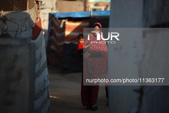 A displaced Palestinian woman is carrying her child and walking at a camp for displaced Palestinians in Deir al-Balah, in the central Gaza S...