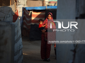 A displaced Palestinian woman is carrying her child and walking at a camp for displaced Palestinians in Deir al-Balah, in the central Gaza S...