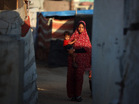 A displaced Palestinian woman is carrying her child and walking at a camp for displaced Palestinians in Deir al-Balah, in the central Gaza S...