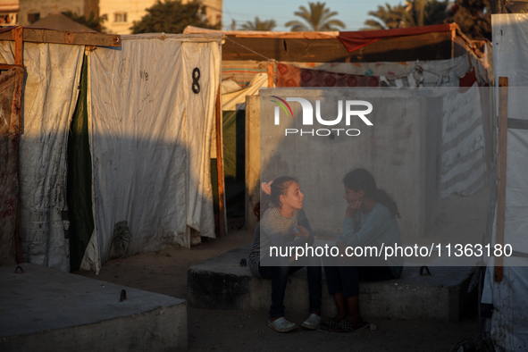 Displaced Palestinian girls are sitting at a camp for displaced Palestinians in Deir al-Balah, in the central Gaza Strip, on June 26, 2024,...