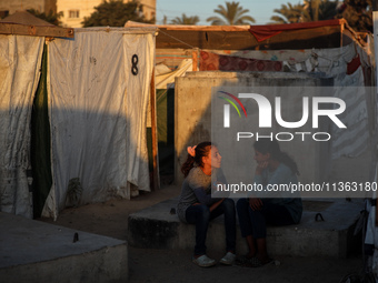 Displaced Palestinian girls are sitting at a camp for displaced Palestinians in Deir al-Balah, in the central Gaza Strip, on June 26, 2024,...