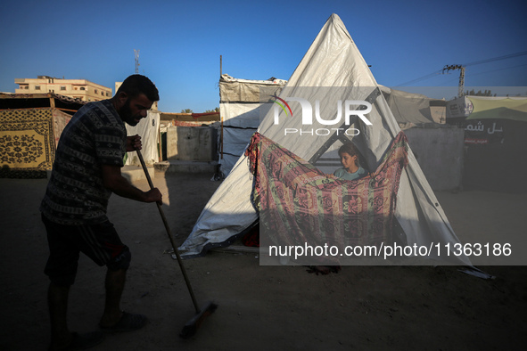 A displaced Palestinian girl is looking outside her tent as her father is sweeping in front of the tent at a camp for displaced Palestinians...