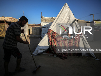 A displaced Palestinian girl is looking outside her tent as her father is sweeping in front of the tent at a camp for displaced Palestinians...