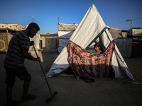 A displaced Palestinian girl is looking outside her tent as her father is sweeping in front of the tent at a camp for displaced Palestinians...