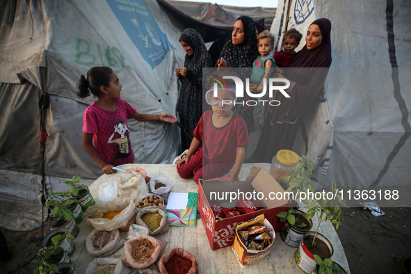 A displaced Palestinian girl is sitting on a stall selling biscuits, spices, and agricultural seedlings at a camp for displaced Palestinians...